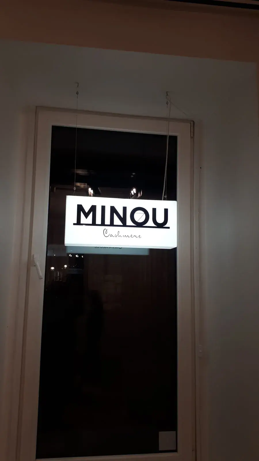 Podświetlany kaseton z logo sklepu MINOU w drzwiach witryny nocą